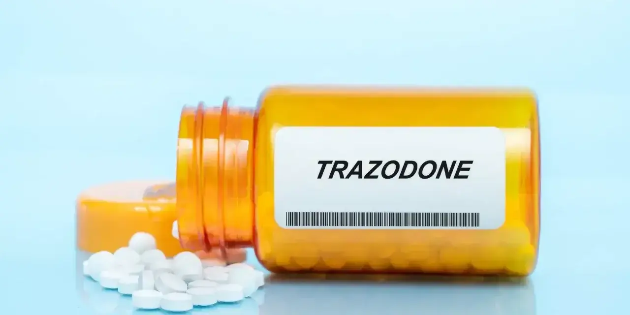 Pomarańczowa butelka leku trazodon, z kilkoma białymi tabletkami rozsypanymi obok.
