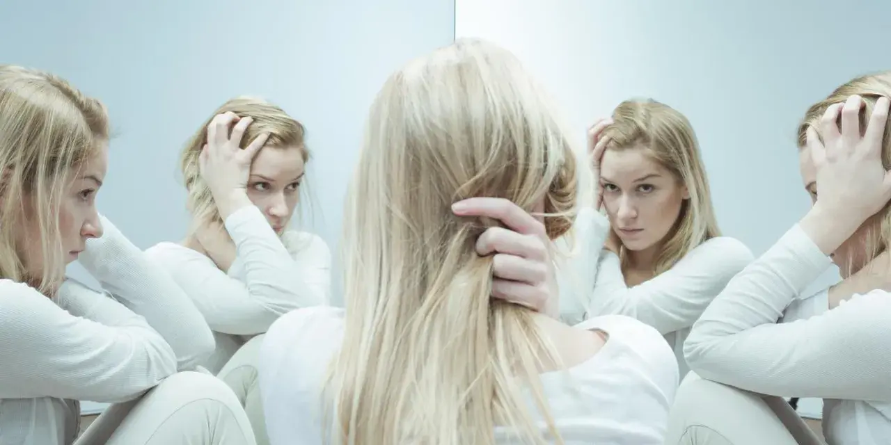 Blondynka w białej bluzie, zmagająca się z kwetaplex, widzi swoje odbicia w lustrze, każde z innym wyrazem twarzy.