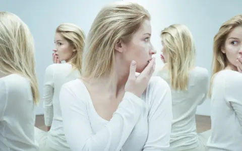 Kobieta z blond włosami w białej bluzce, otoczona swoimi odbiciami w lustrze.