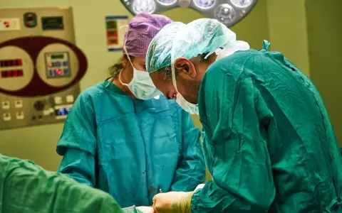 Chirurdzy w maseczkach i czepkach przygotowują się do operacji. Narkoza już działa, pacjent jest bezpieczny.