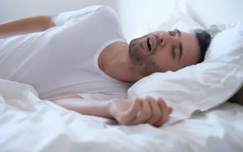 Mężczyzna śpi na boku, z otwartymi ustami i widocznym chrapaniem.