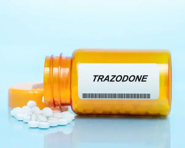 Pomarańczowa butelka leku trazodon, z kilkoma białymi tabletkami rozsypanymi obok.